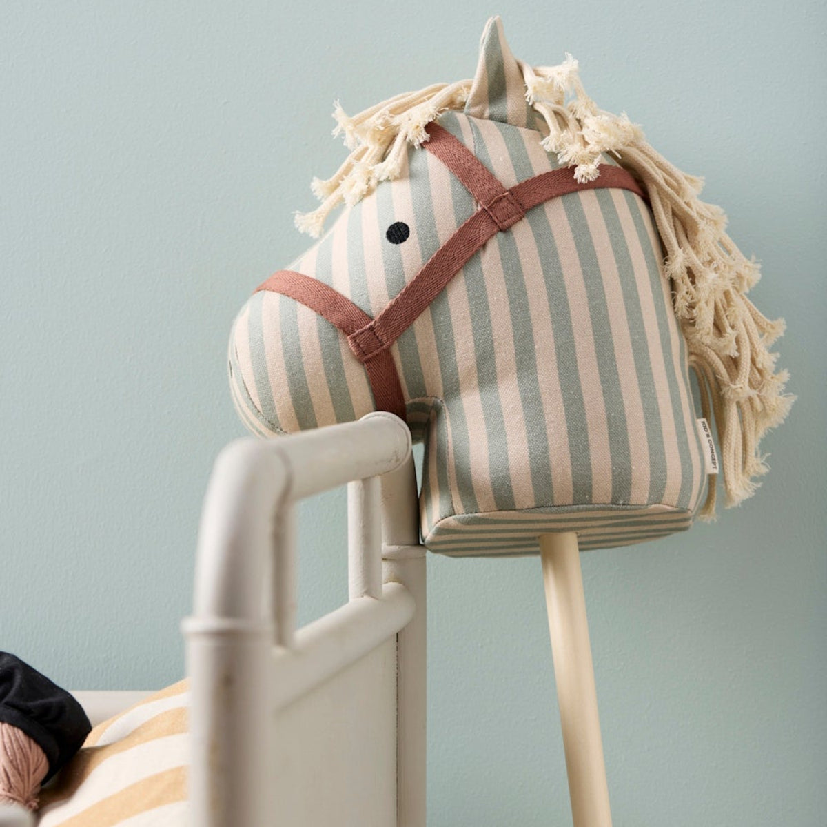 Close-up of a striped fabric hobby horse leaning against the wooden frame of a crib.