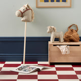 Striped fabric hobby horse next to a matching toy horse, book, and storage bench.