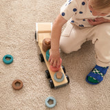 Child playing on a beige carpet with a wooden sorting truck toy holding colorful rings.