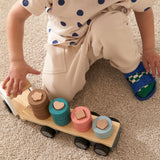 A toddler playing on a rug with a wooden shape-sorting toy truck with colorful stacked rings.