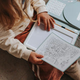 A child holding a drawing sheet over a light-up drawing pad in their lap.
