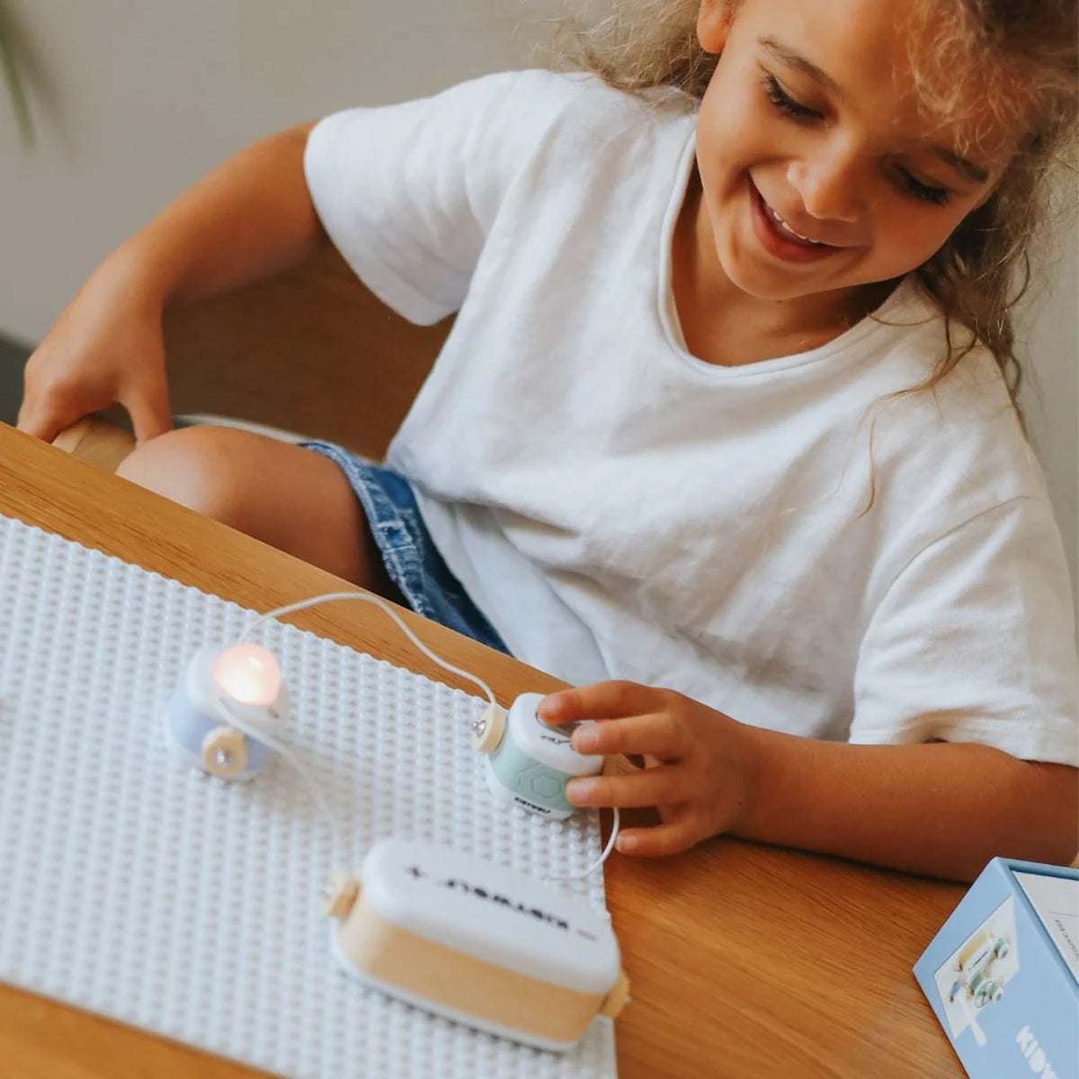 A smiling child playing with a toy electrical science kit that has a small glowing light block.