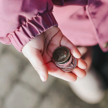 Close-up of a child's open hand holding three toy coins featuring animal illustrations.