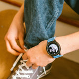 Close-up of a person tying grey sneakers while wearing a black smartwatch with a light blue strap.