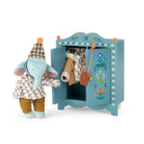 Plush elephant doll next to a blue wooden toy wardrobe filled with doll clothes.