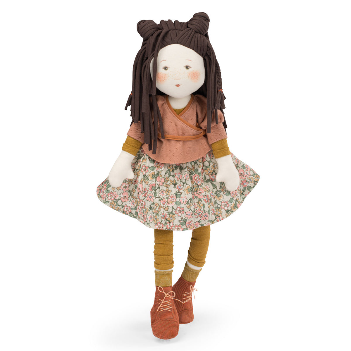 A plush doll with brown braided hair in two buns, wearing a peach top, floral skirt, yellow socks, and orange shoes. The doll's face is cheerful.