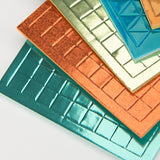 Stacked colorful metallic textured tiles with grid and geometric patterns on a white background.