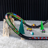 Candylab toy cars racing on a wooden track with banked turns and stylized pine trees on a rug.