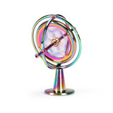 Rainbow metal gyroscope spinning top balancing on its matching stand against a plain white background.
