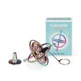 Moulin Roty iridescent metal gyroscope toy with string and stand next to its illustrated blue box.