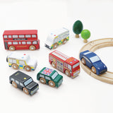 Seven wooden London toy vehicles with wooden trees and a track section on a white background.