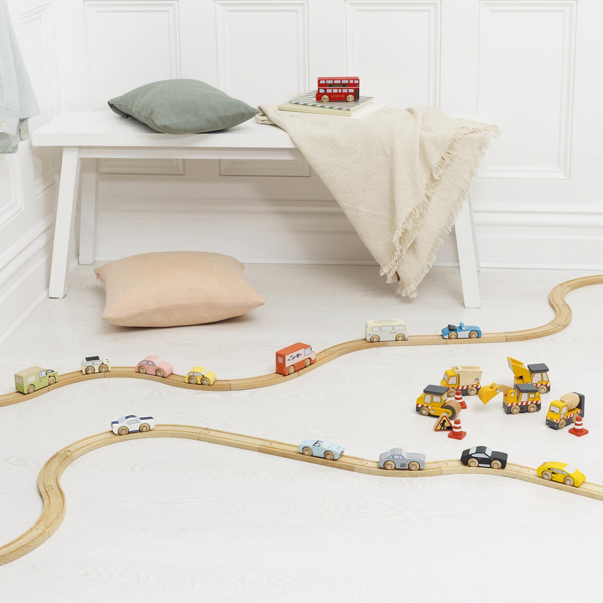Wooden toy cars driving along wooden tracks spread out in a bright playroom.