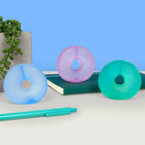 Three cool-toned gel stress loops displayed on a desk with a notebook, pen, and potted plant.