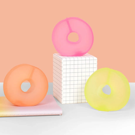 Three colorful ring-shaped gel stress toys displayed on grid pedestal and pastel notebooks.