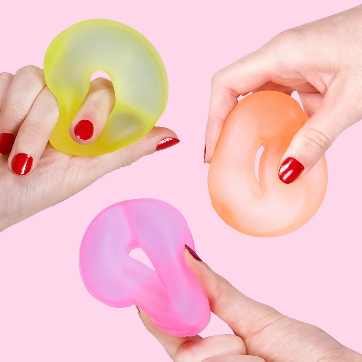 Three hands squeezing squishy, colorful ring-shaped memory gel stress toys.