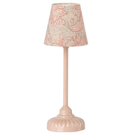 A vintage-style table lamp with a soft pink base and stem. The lampshade features a light blue fabric with intricate red floral patterns, set against a white background.