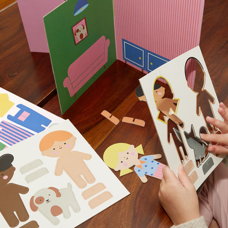 Child’s hands popping out character figures from a cardboard sheet next to a 3D toy house set.