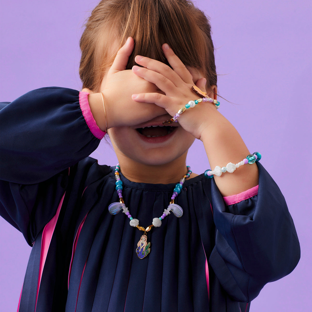 Girl wearing Coralie mermaid collection beaded bracelet and matching mermaid charm necklace with seashell beads.