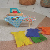 Wooden toy iron and ironing board set with colorful felt doll clothes on a play room rug.