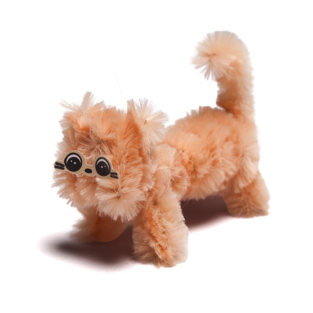 A tiny, fuzzy orange cat craft made from pipe cleaners with sticker eyes, standing on a white background.