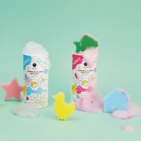 Two colorful bath salt containers overflow with foam against a mint green background. Sponges shaped like a star, duck, and house add playful elements.