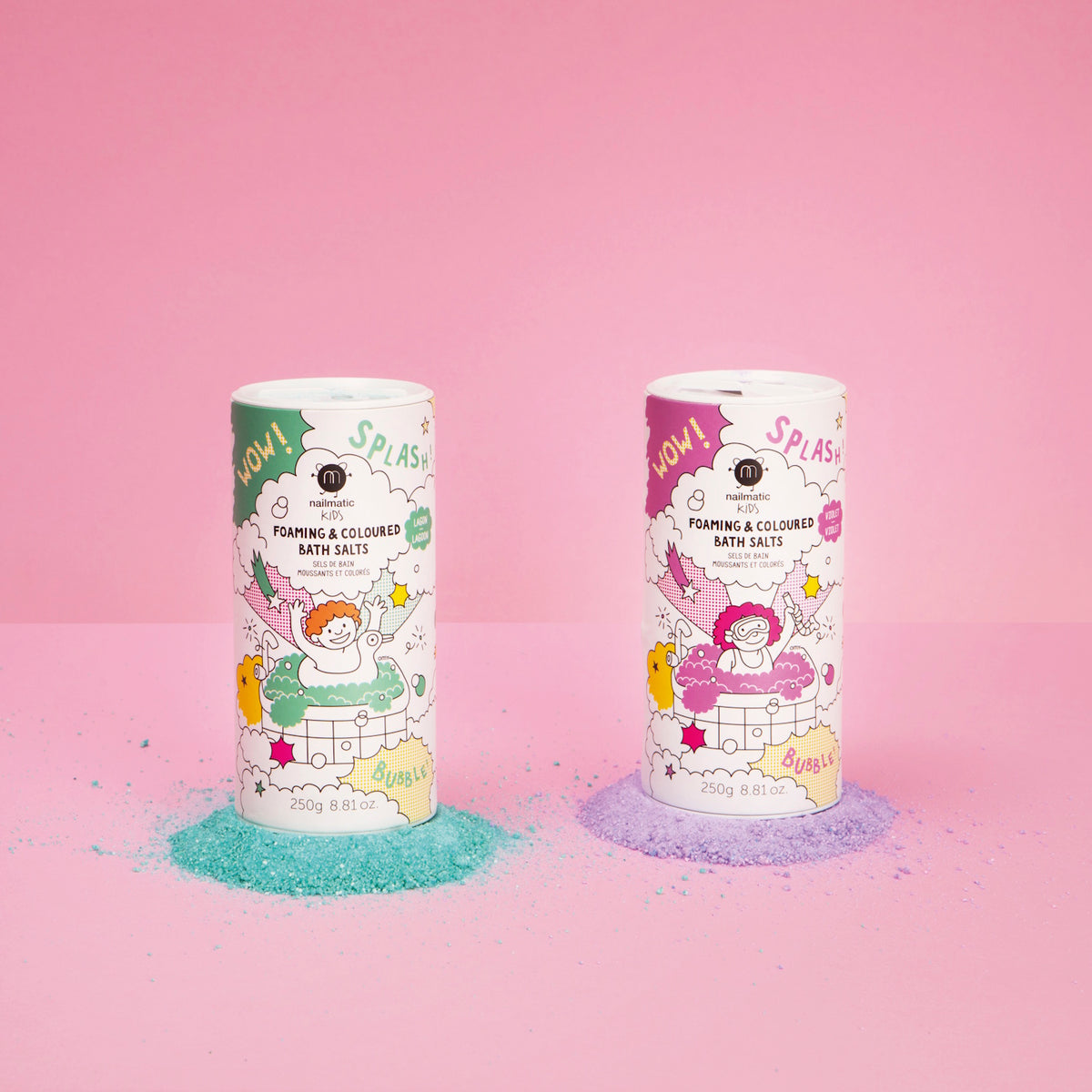 Two cylindrical containers of foaming bath salts stand on a pink background. One has green illustrations with spilled blue powder; the other has pink illustrations with spilled purple powder. Both feature playful graphics, creating a fun, vibrant mood.