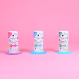 Three colorful bath salt containers on a pink background, each surrounded by matching colored salts, purple, blue, and green. Playful packaging with cartoon graphics conveys a fun, vibrant tone.