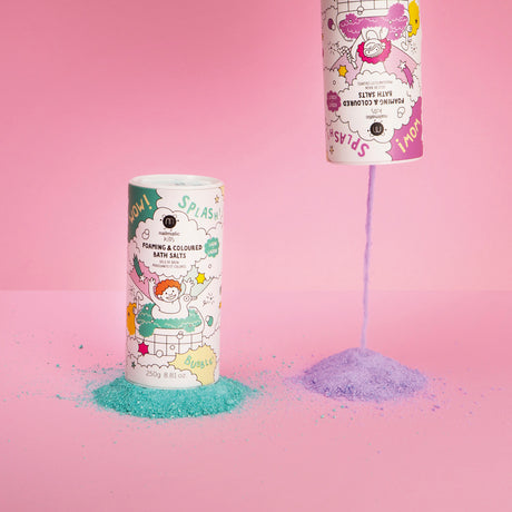 Two colorful bath salt containers on a pink background. One upright with green salts, the other pouring purple salts, creating playful mounds.