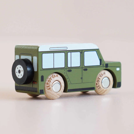 Rear three-quarter view of a green wooden toy car with a spare tire mounted on the back.
