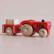 Red wooden toy tractor with a matching trailer carrying a hay bale, shown in a side view.