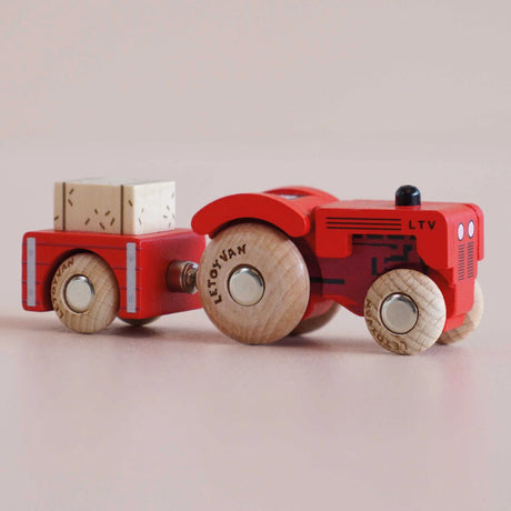 Red wooden toy tractor with a matching trailer carrying a hay bale, shown in a side view.