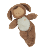 A plush toy with a brown, fluffy dog feature, closed eyes, and a serene expression. It features a white belly with a small embroidered rainbow.