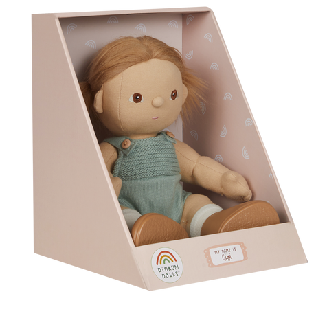A soft doll with brown hair in pigtails sits in a pastel box. The doll wears a knitted green romper and is labeled "Gigi" with a cheerful expression.