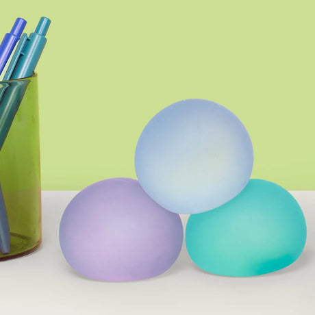 Three cool-toned memory gel stress balls stacked on a desk next to a pencil cup.