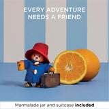 Wooden Paddington Bear figure holding a jar and suitcase next to real oranges with text "Every adventure needs a friend".