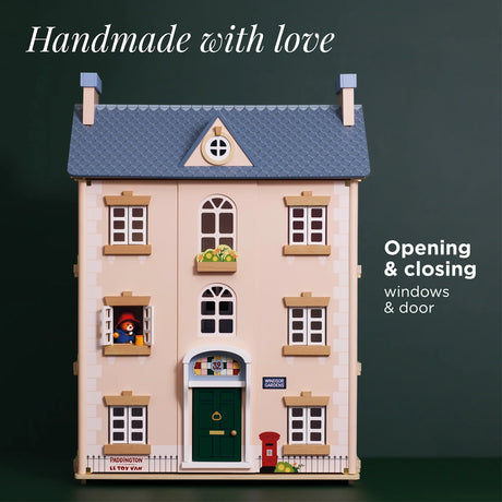 Wooden dollhouse featuring a blue roof, green front door, and Paddington looking out an open window.