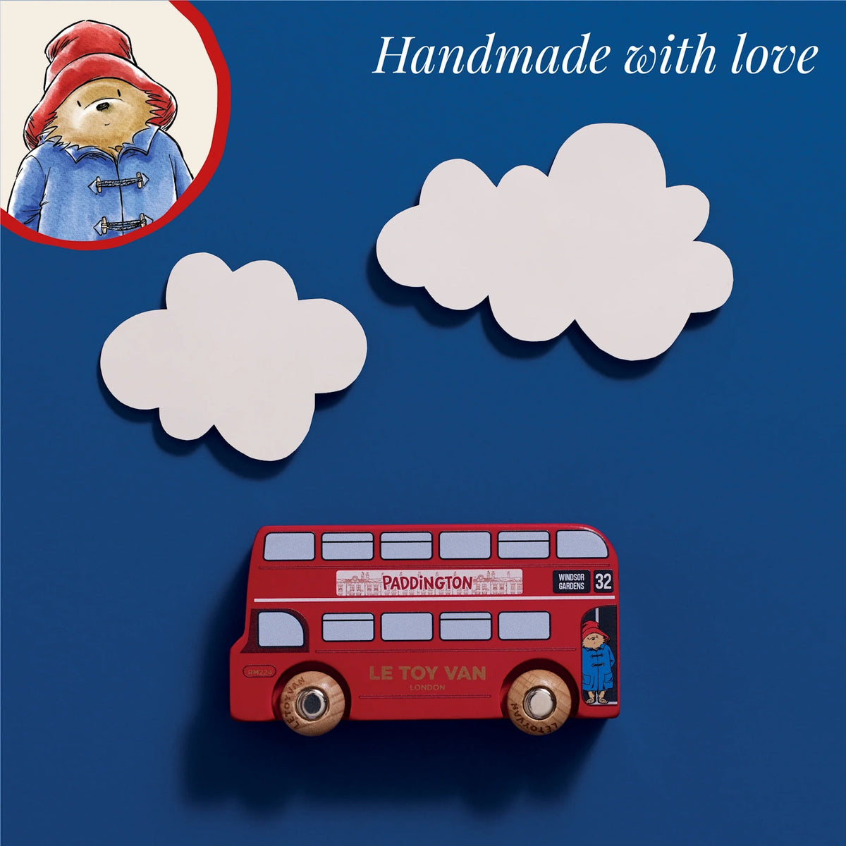 Paddington toy bus on blue background with white clouds, an illustrated bear inset, and "Handmade with love" text.