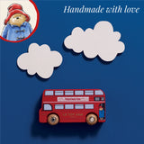 Paddington toy bus on blue background with white clouds, an illustrated bear inset, and "Handmade with love" text.