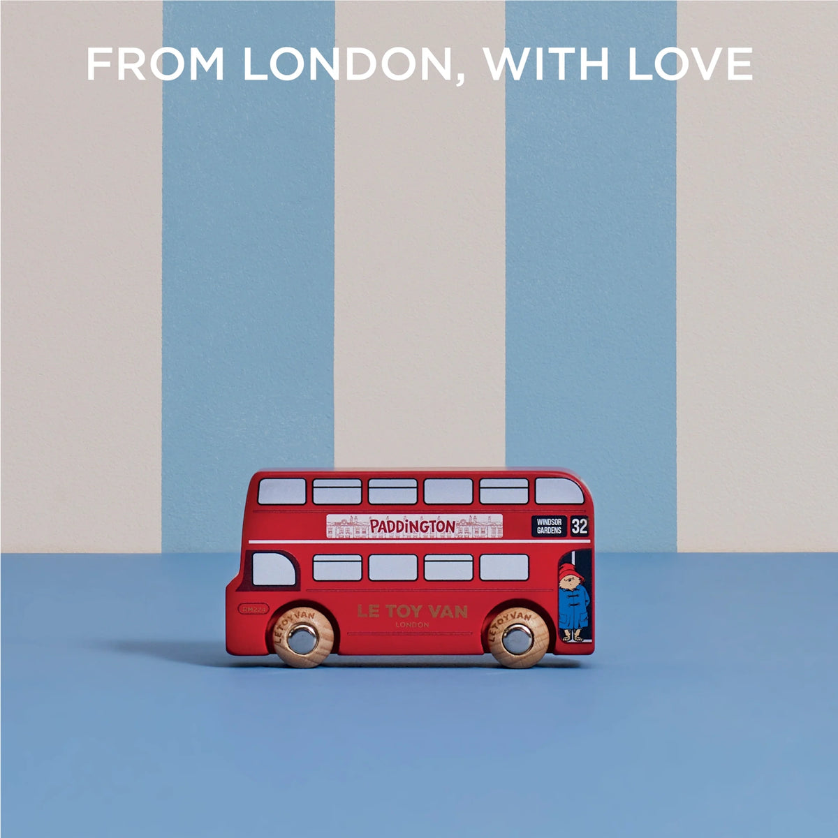 Paddington toy bus on a blue surface against a striped background, with text reading "FROM LONDON, WITH LOVE".