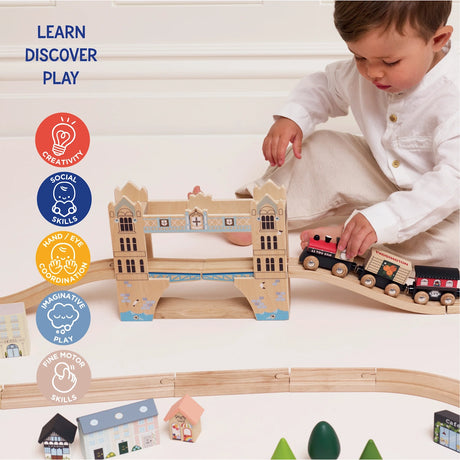 A toddler playing with a wooden train moving across a bridge in a wooden toy train set track.