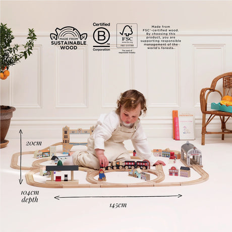 A child playing on the floor with a wooden train set, featuring overlaid dimensions and sustainability logos.