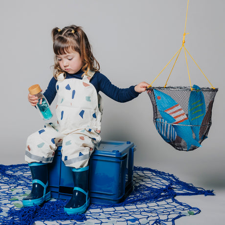 Girl holding a sensory bottle while reaching for a hanging net filled with toys.