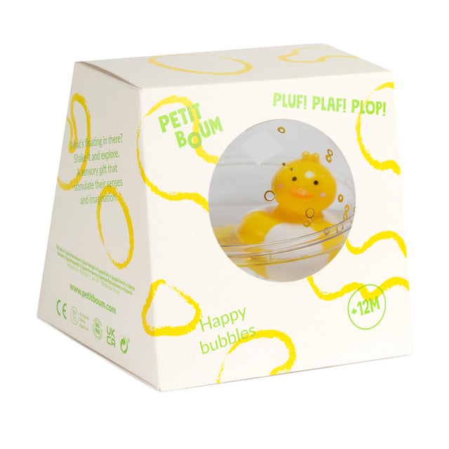 White box with a circular window revealing a floating yellow duck in clear liquid. Box features yellow wavy lines, text reads "Petit Boum," "Happy bubbles," and is for ages 12 months and up.