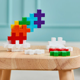 Colorful interlocking puzzle pieces stacked on a wooden table against a light blue wall. Brightly colored blocks create a playful, creative scene.