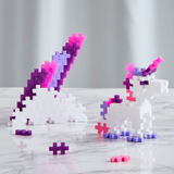 A white unicorn and mountain built from pink, purple, and white glitter Plus-Plus blocks on a marble surface.