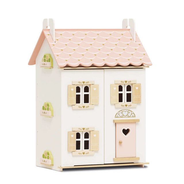 Wooden dollhouse with a pink scalloped roof and white walls. Features windows with tan shutters, heart details, and a pink door, creating a charming, cozy feel.