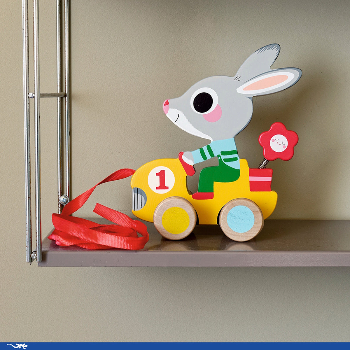 Wooden bunny pull toy in a yellow race car with red ribbon, sitting on a shelf.