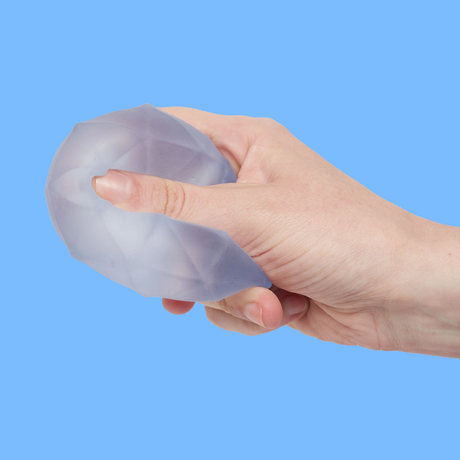 A hand squeezing a translucent, geometric-patterned stress ball against a light blue background, conveying a sense of calm and stress relief.