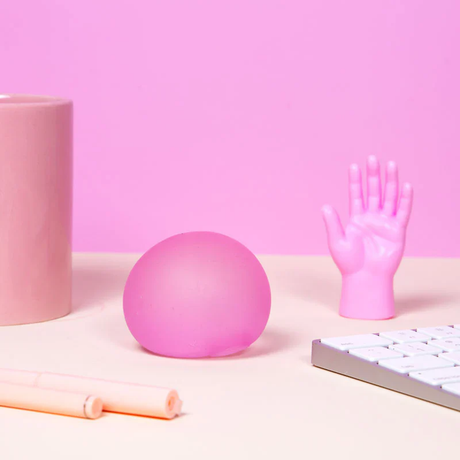 A pastel workspace features a pink stress ball, a small pink hand sculpture, and a white keyboard on a light beige surface, exuding a playful, calm vibe.