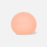 A soft, rounded, peach-colored stress ball with "SPEKS" subtly embossed on the front. The background is white, conveying a calm, minimalistic tone.